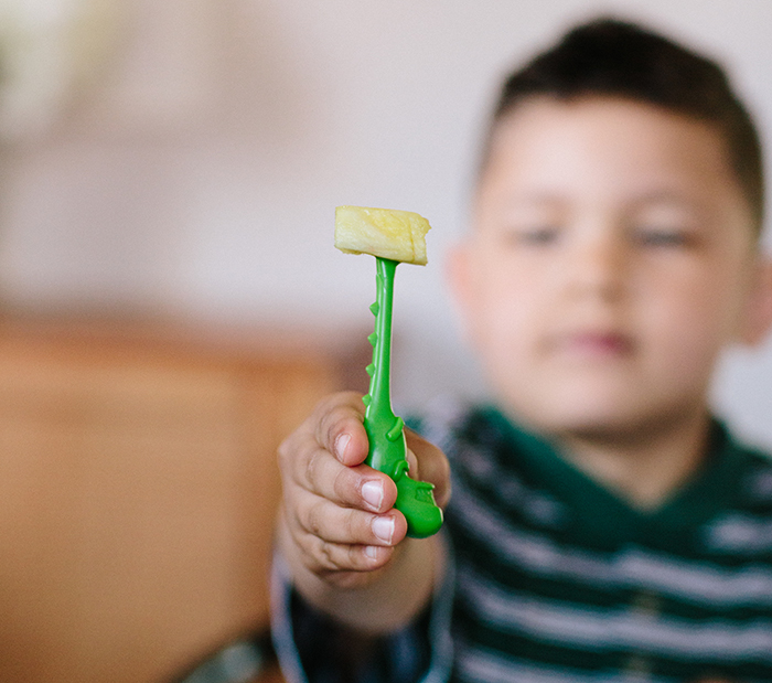 A child is shown holding a green character pick with a slice of pineapple on it.