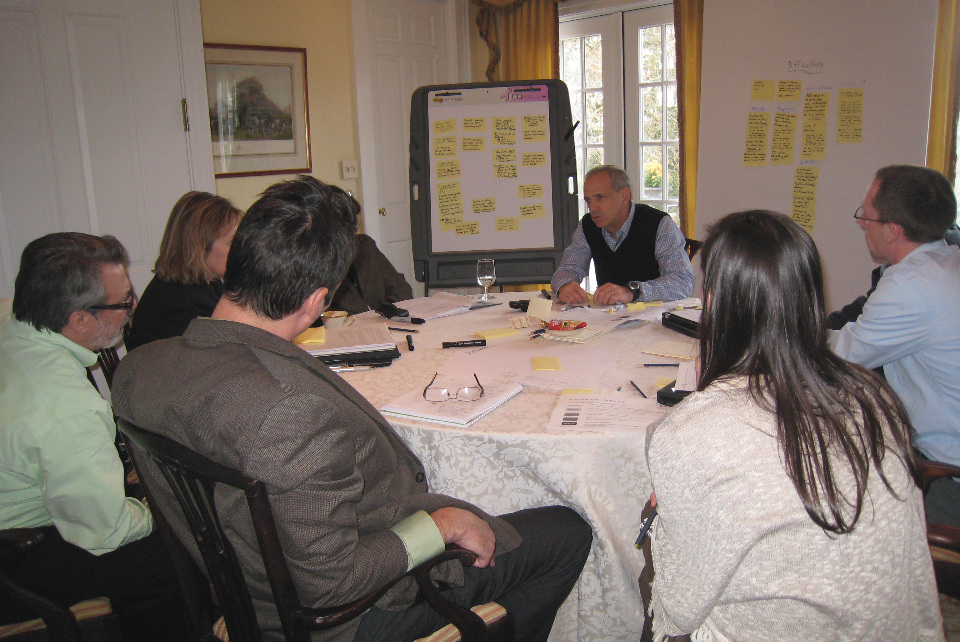 People gather around a table ideating for the session, while surrounded by easels filled with sticky notes.