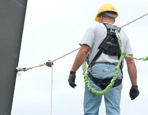 A construction worker is shown wearing the fall safety harness while connected to a safety line.