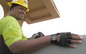 A smiling construction worker in a green high-visibility shirt and a yellow hard hat is pictured wearing black construction gloves.