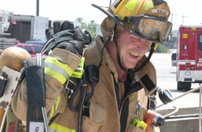 A firefighter is shown wearing an SBCA and other gear, with a fire truck in the background.