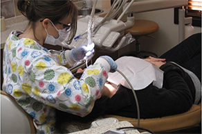 A dental hygienist is shown in a dental office cleaning the teeth of a patient who's identity is obscured.