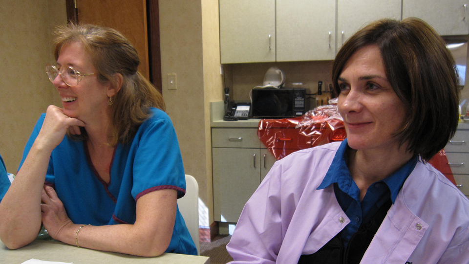 Two dental hygienists sit at a table in a dental office, answering questions put to them by the Daedalus Research Manager who is off screen.