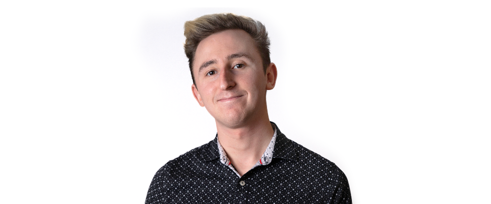 A headshot of Harry on a white background. Harry is wearing a dark gray shirt with a geometric pattern and a light gray collar.