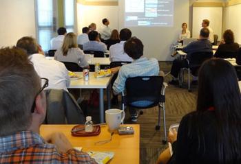 People sit at tables in front of a projector screen listening to a panel of speakers.