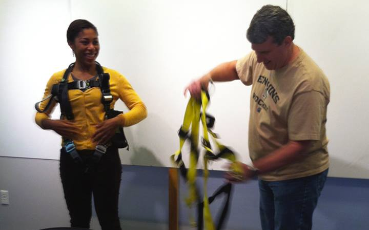 Two people try on safety harnesses: one is fully wearing the Daedalus-designed harness and watching the other person attempt to don a generic harness.