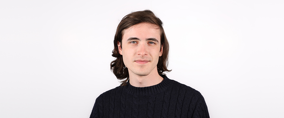 A headshot of Chris is shown on a light gray background. Mitcham is wearing a black crew neck shirt.